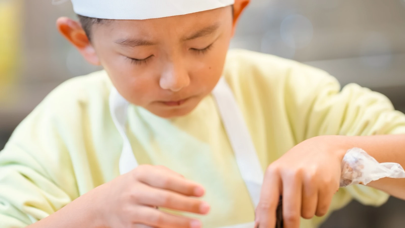 A young boy in a chef hat concentrating as he decorates his creation
