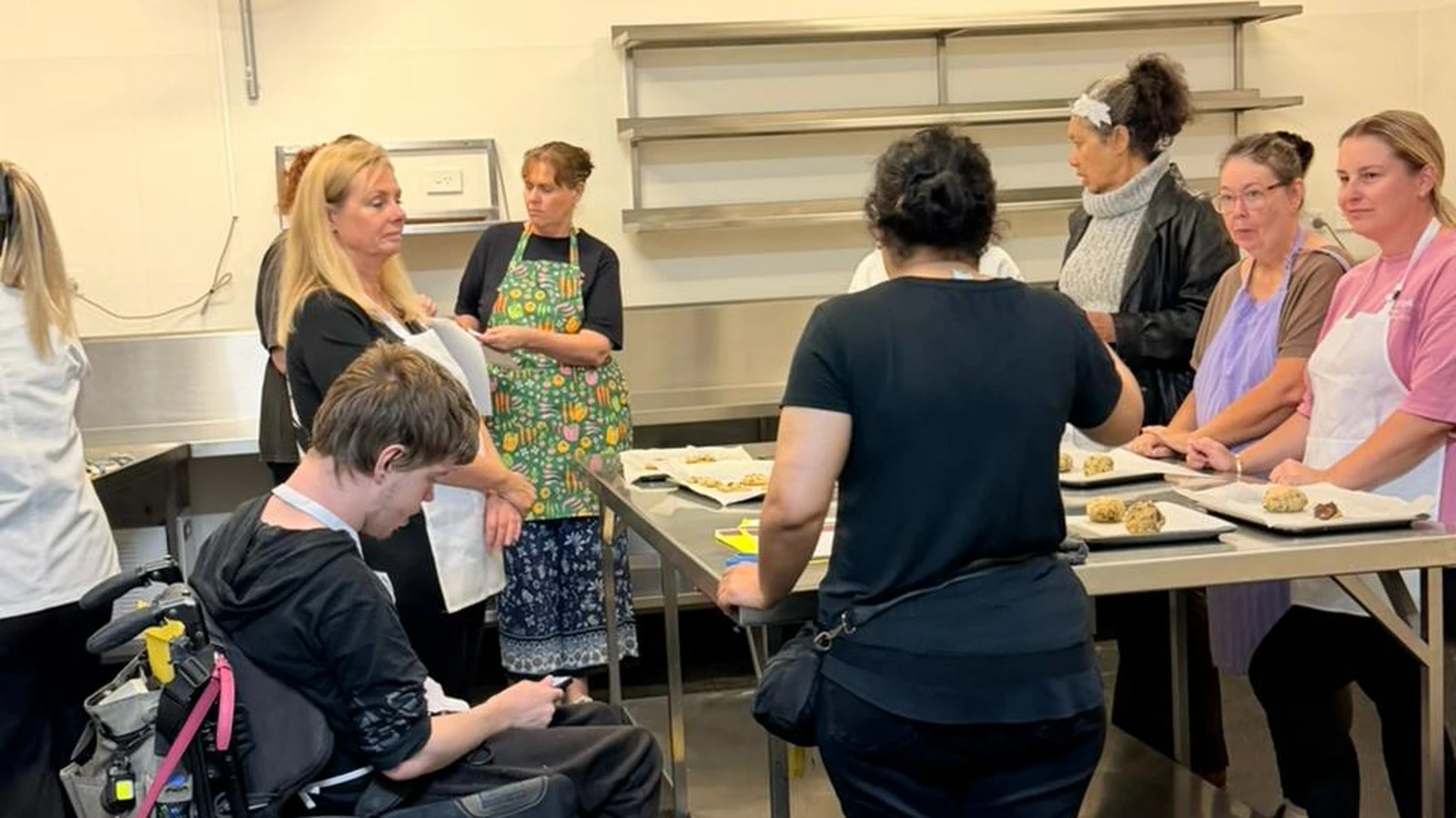 Adults gathered around a kitchen bench with trays of freshly baked cookies