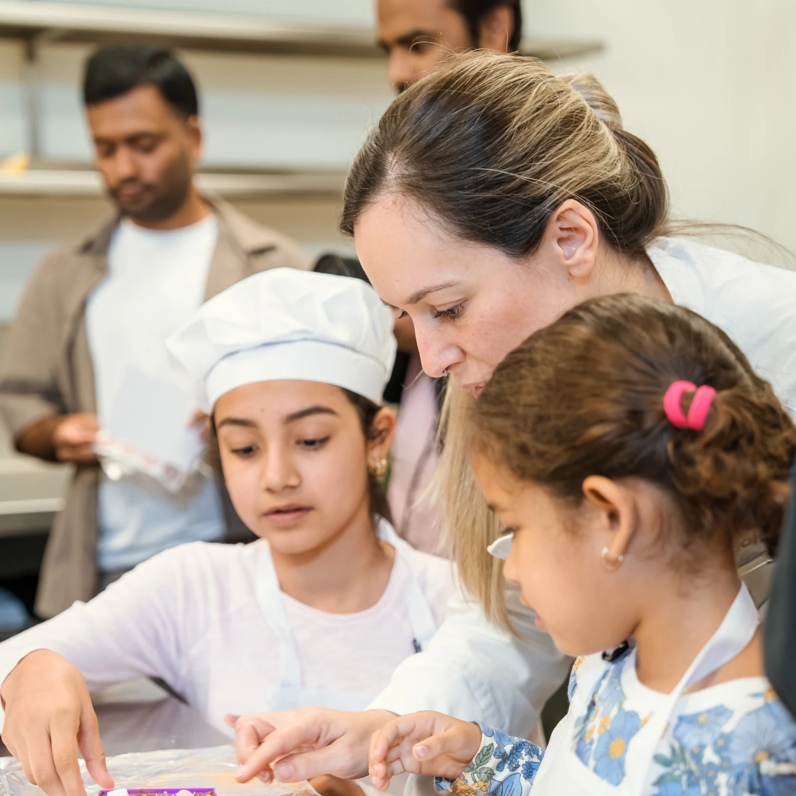 A chef guiding two young girls as they decorate their creations