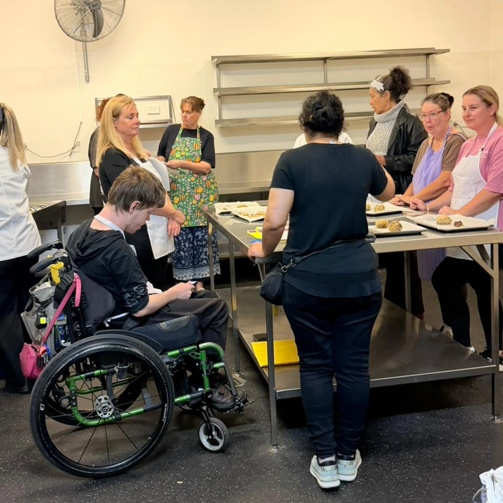 Participants around a kitchen bench with trays of freshly baked cookies, one of them using a wheelchair